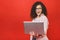 Portrait of an excited curly young girl holding laptop computer isolated over red background