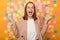 Portrait of excited extremely happy businesswoman wearing beige jacket standing against yellow wall with colorful memo cards,