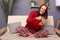 Portrait of excited, extremely woman with dark hair wearing home clothing sitting on sofa in living room, holding mobile phone in