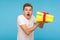 Portrait of excited man in t-shirt looking at camera with shocked face and holding unpacked gift box