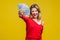 Portrait of excited rich beautiful woman in red dress holding money, isolated on yellow background