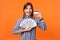 Portrait of excited rich brunette woman wearing checkered shirt holding dollar bills. indoor studio shot isolated on orange