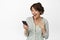 Portrait of excited and surprised young woman looking at mobile phone happy, laughing amazed at message, standing