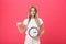 Portrait of an excited young girl dressed in white t-shirt pointing at alarm clock and looking at camera over