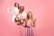 Portrait of excited young lady with bunch of balloons for birthday or Woman`s Day, celerating holiday on pink background