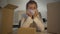 Portrait of exhausted young tailor in face mask sitting at the table with cardboard boxes and thinking. Camera