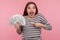 Portrait of extreme overjoyed delighted young woman in striped sweatshirt screaming in excitement and pointing dollar bills