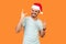 Portrait of extremely happy bearded young man in santa hat and casual white t-shirt standing with closed eyes, showing rock and