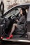 portrait of fabulous brunette wearing checkered dress and red high-heeled shoes in a lux car. woman in automobile.