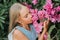 Portrait face of candid little kid girl of eight years old on background of green plants and admired enjoy smell pink flowers duri