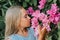 Portrait face of candid little kid girl of eight years old on background of green plants and admired enjoy smell pink flowers duri