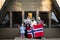 Portrait of family with kids outside cabin house holding Norway flags. Scandinavian culture, norwegian people