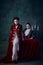 Portrait of fantastic woman and man in medieval costumes over dark green background. Vampire look. Lord Dracula