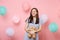 Portrait of fascinating joyful young woman in blue dress holding and hugging teddy bear plush toy on pink background