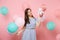 Portrait of fascinating woman in blue dress looking on red box with gift present holding colorful air balloons on pink