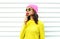 Portrait fashion pretty cool girl sucking lollipop in colorful clothes over white background wearing pink hat yellow sunglasses