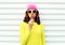 Portrait fashion pretty cool girl sucking lollipop in colorful clothes over white background wearing a pink hat yellow sunglasses