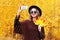 Portrait fashion smiling young woman taking autumn picture makes self portrait on smartphone over sunny yellow leaves