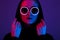 Portrait of fashion young girl in a black sweater with a hood and round sunglasses in red and blue neon light in the