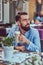 Portrait of a fashionable bearded male with a stylish haircut, drinks a glass of a cappuccino, sitting in a cafe