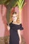 Portrait of Fashionable Caucasian Blond Girl in Black Dress. Posing Near Tree Indoors