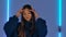 Portrait of fashionable model posing in dark studio against backdrop of bright neon lights. Pretty young woman in blue