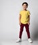 portrait of fashionable preschool little boy in yellow t-shirt, red denim pants, white sneakers, standing isolated on