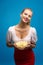Portrait of fashionable young blond woman in pink-red dress, bright make-up holding, eating fried potato, chips and over