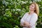 Portrait of a fat plump young blonde woman blooming with an apple tree on a white floral background in a park on a spring day.