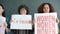 Portrait of female activists holding banners demanding gender equality screaming standing against grey background