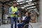 Portrait of female manager in wheelchair working in warehouse, talking with logistics employee. Concept of workers with