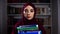 Portrait of a female Muslim professor standing on a bookshelf background and holding folders