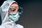 Portrait of female nurse in medical mask with safety glasses and in white protective suit on grey background
