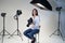 Portrait Of Female Photographer In Studio For Photo Shoot With Camera And Lighting Equipment