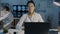 Portrait of female practitioner in white gown sitting at desk with laptop in dark hospital office