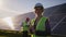 Portrait of a female solar engineer standing looking at the camera, another man near the panels and entering information