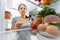 Portrait of female standing near open fridge full of healthy food. Portrait of female
