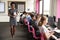 Portrait Of Female Teacher Holding Digital Tablet Teaching Line Of High School Students Sitting By Screens In Computer Class