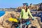 Portrait of female tourist cyclist on the rocky shore on the lighthouse background