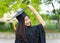 Portrait of a female university graduate wears black academic gown and hat, holds degree certificate with joyful moment after