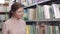 Portrait of focused college girl looking for a book among bookcases