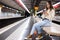 Portrait of a focused girl sitting on a subway platform bench with a mobile phone