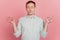 Portrait of focused healthy fit concentrated guy hold fingers close eyes meditate on pink background