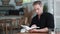 Portrait of focused man in black shirt sits in modern outdoor cafe, reads book