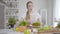 Portrait of focused young girl adding sliced ingredients into bowl. Caucasian woman preparing organic salad with