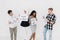 Portrait of four cheerful multiracial friends standing over white wall, looking each other, posing together with