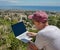 Portrait of a freelancer man working on a laptop on a mountain near a seaside town