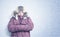 Portrait of a freezing man in winter clothes warming his hands in his sleeves, it is snowing around with the wind.