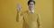 Portrait of friendly Asian man waving hands and smiling looking at camera on yellow background