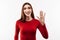 Portrait of friendly woman waving hand, looking at camera with engaging toothy smile. Studio shot, white background